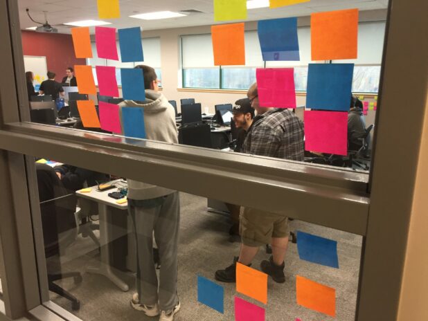 Instructional Designer for eLearning 4 Students seen through a classroom window covered with colorful stickie notes while performing and agile scrum brainstorm